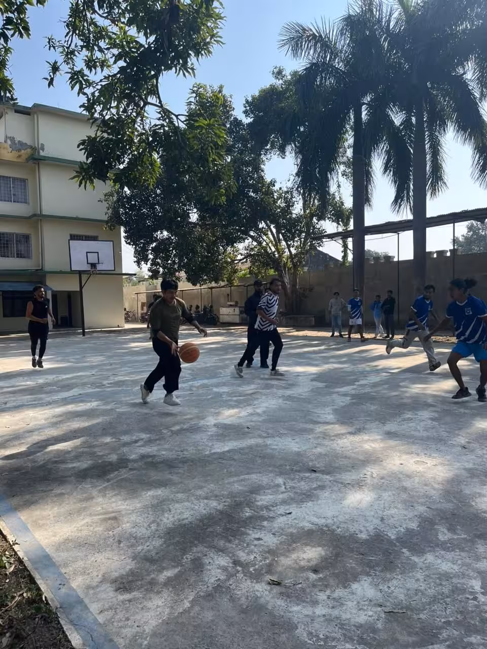 A game on the outdoor basketball court, teaching blocks and palm trees along the far side