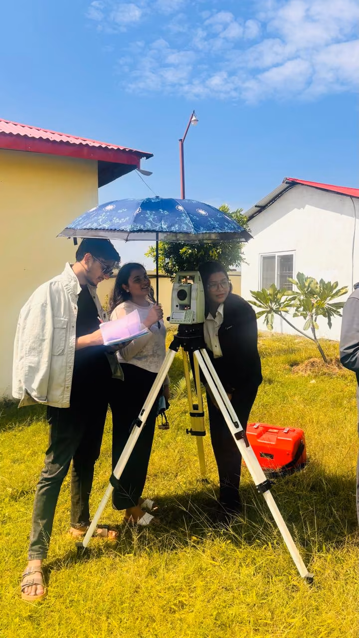 Two students reading a survey instrument under a blue umbrella on the grass