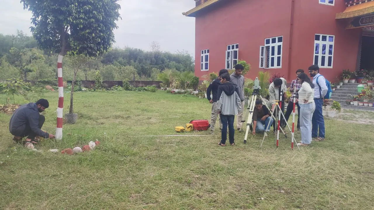 Students setting out with survey tripods on the lawn, the red campus building behind