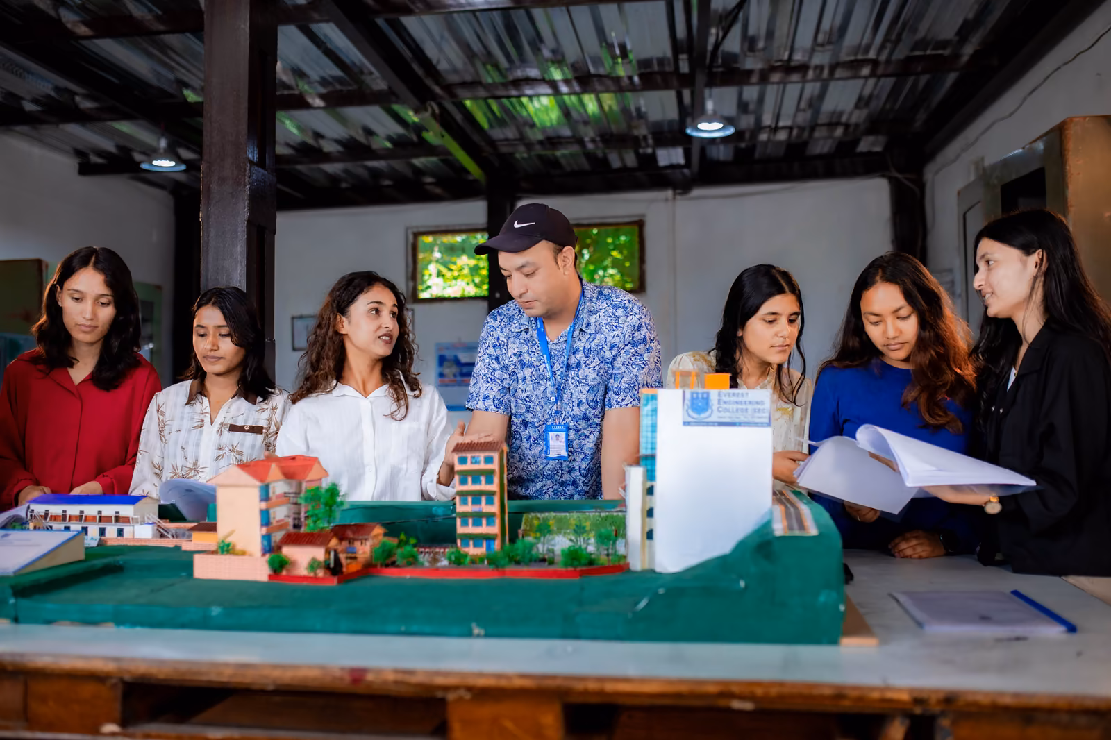 Students and a tutor round a table of architectural scale models, streets and blocks laid out on a base