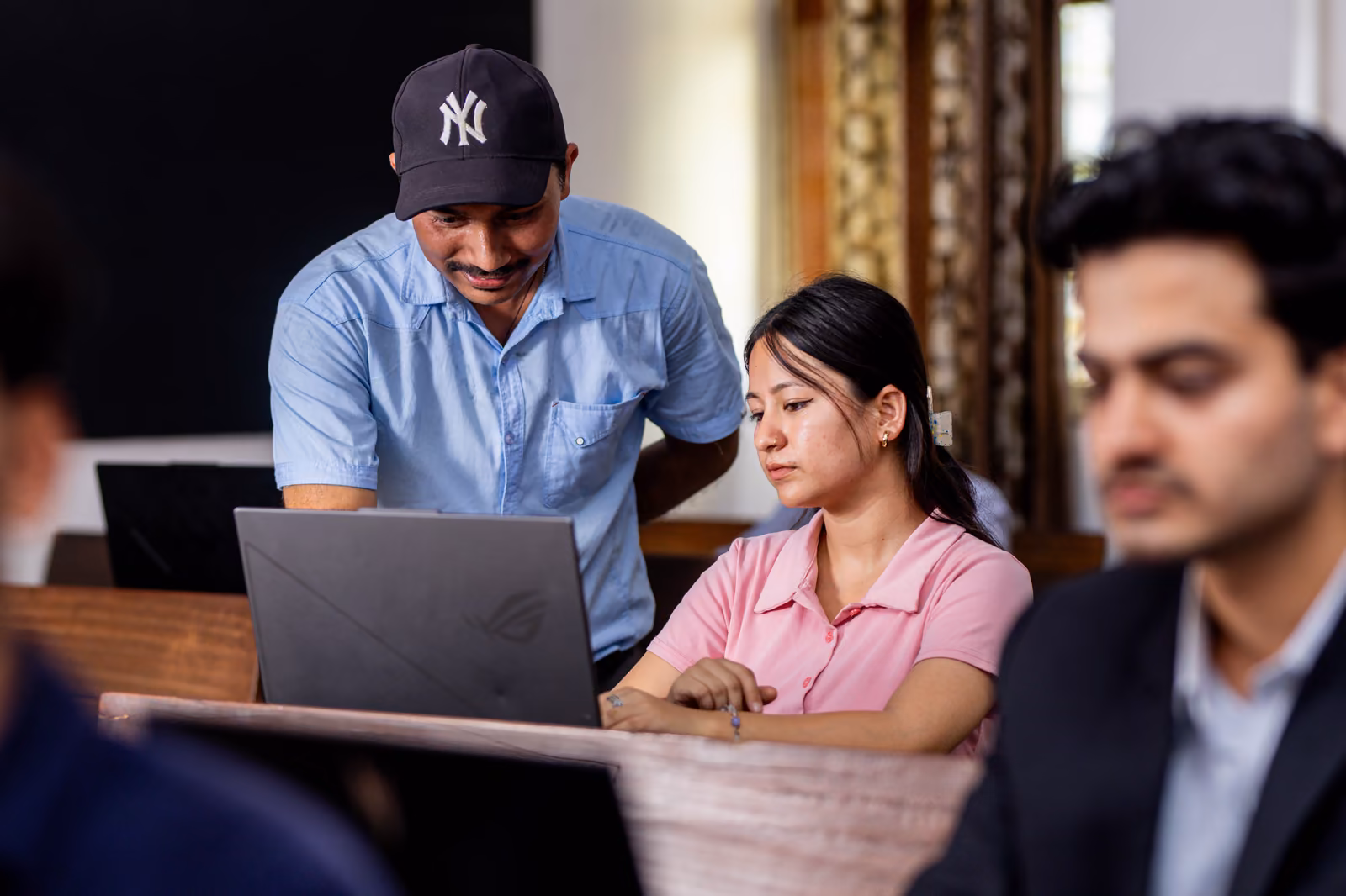 A tutor leaning over a student's laptop at a bench of working students