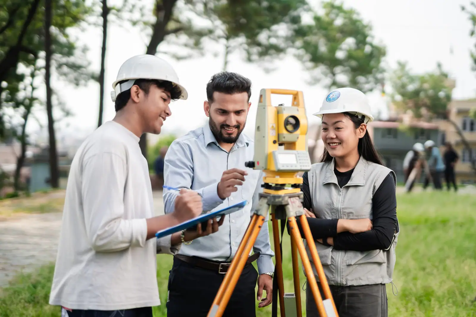 Three students round a total station on the lawn, one entering a reading on a clipboard