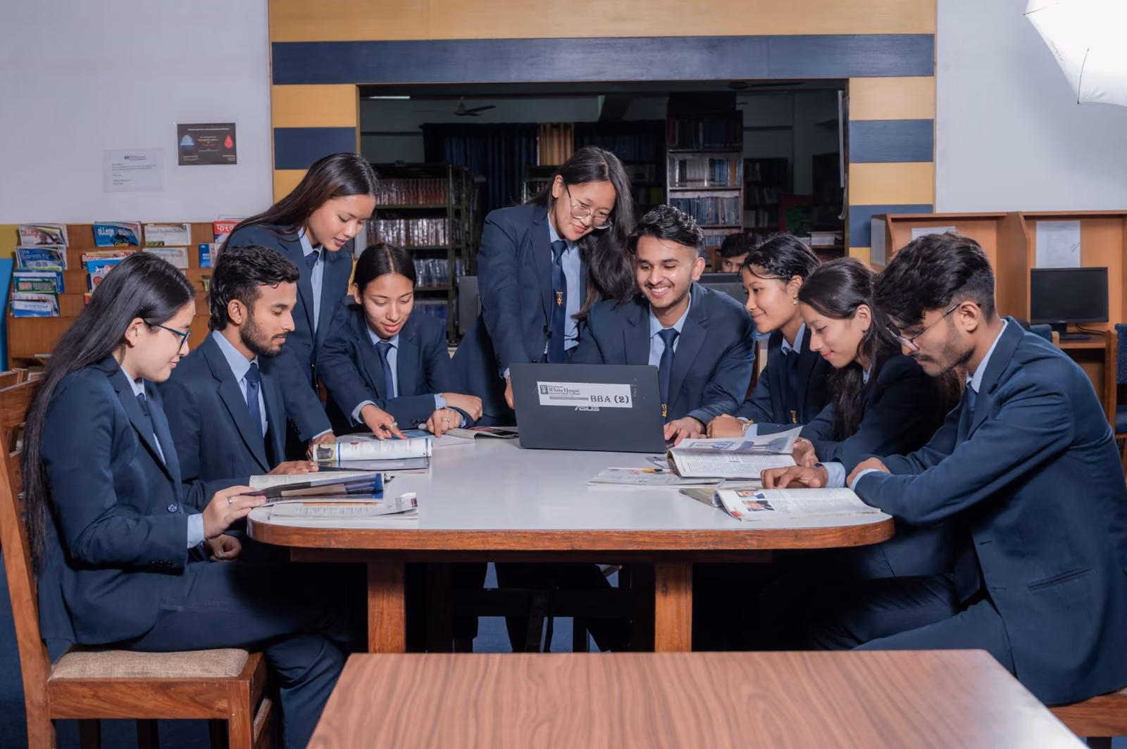 Students working round a table of laptops and books in the library, stacks behind them