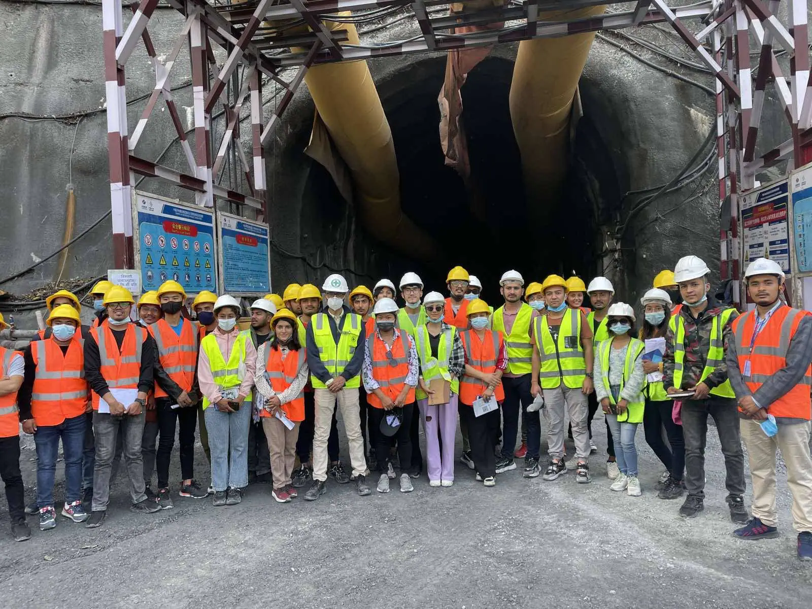 A student group in hi-vis vests and hard hats at a tunnel portal, gantry and hoses above them