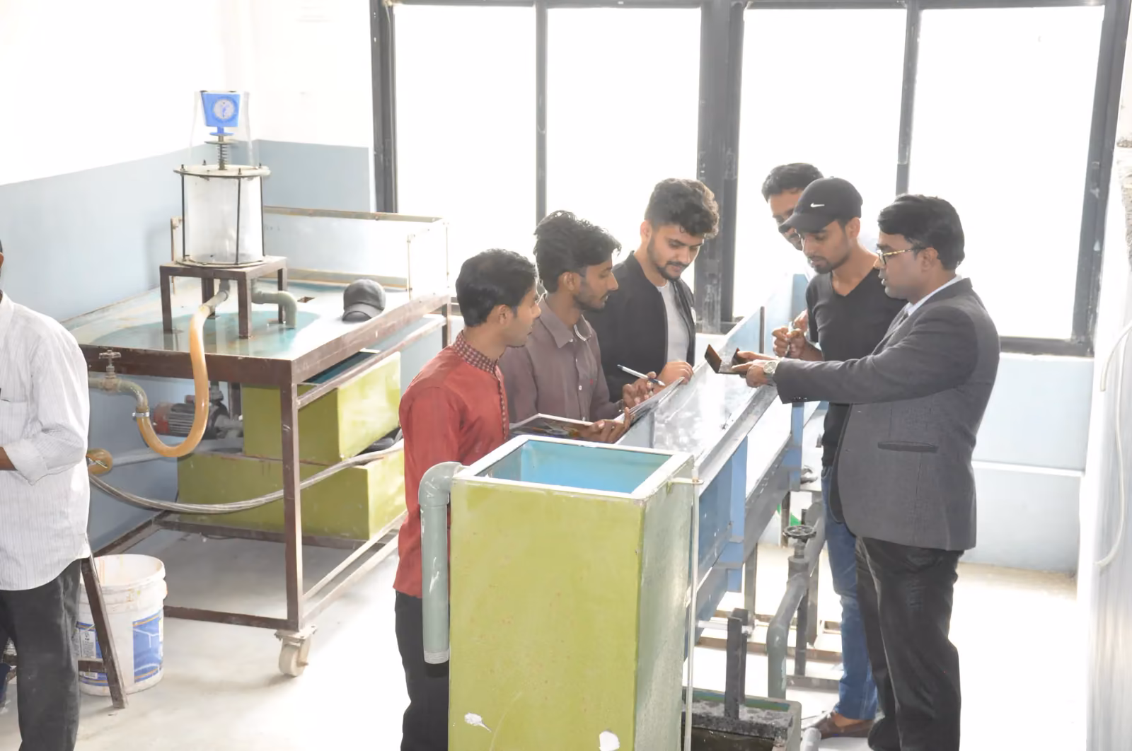 Students round an open water channel in the fluids laboratory, a tutor beside them