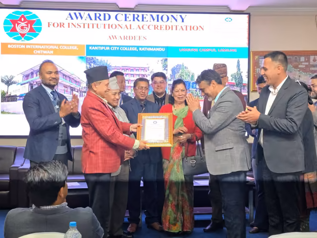 A framed accreditation certificate handed over at a ceremony, the awardees listed on the screen