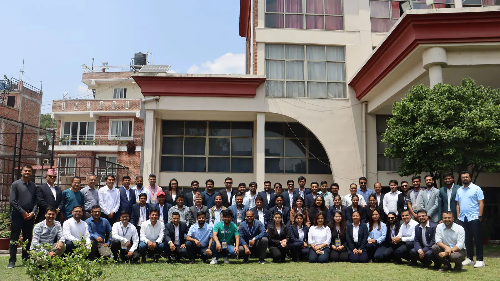 A whole cohort seated and standing on the lawn in front of the college building