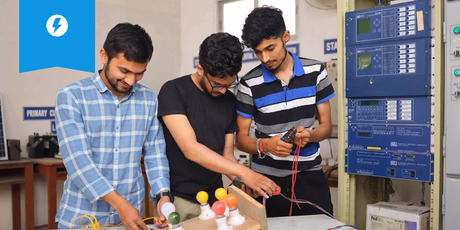 Three students at an electrical panel with a multimeter and leads on the bench