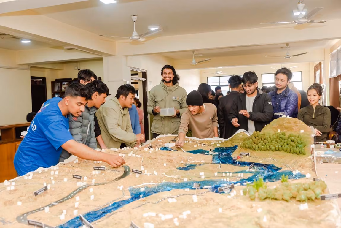 Students crowded round a large relief model of a valley, placing markers on it