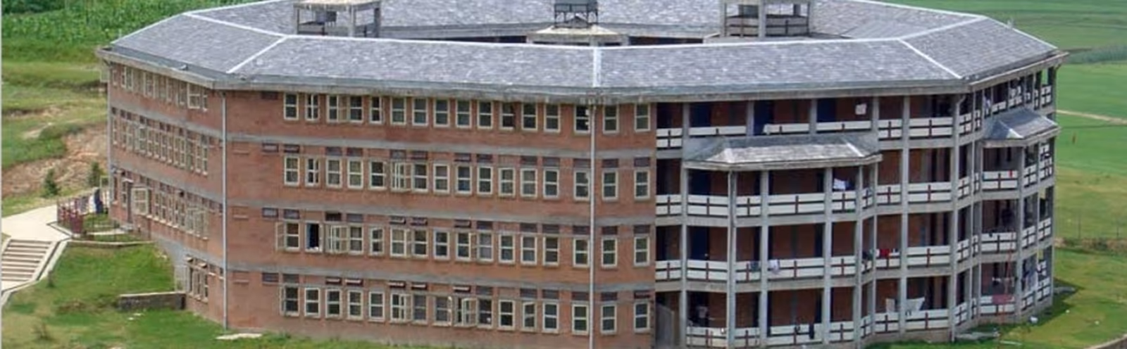 A curved brick teaching block with banded windows, standing above open ground