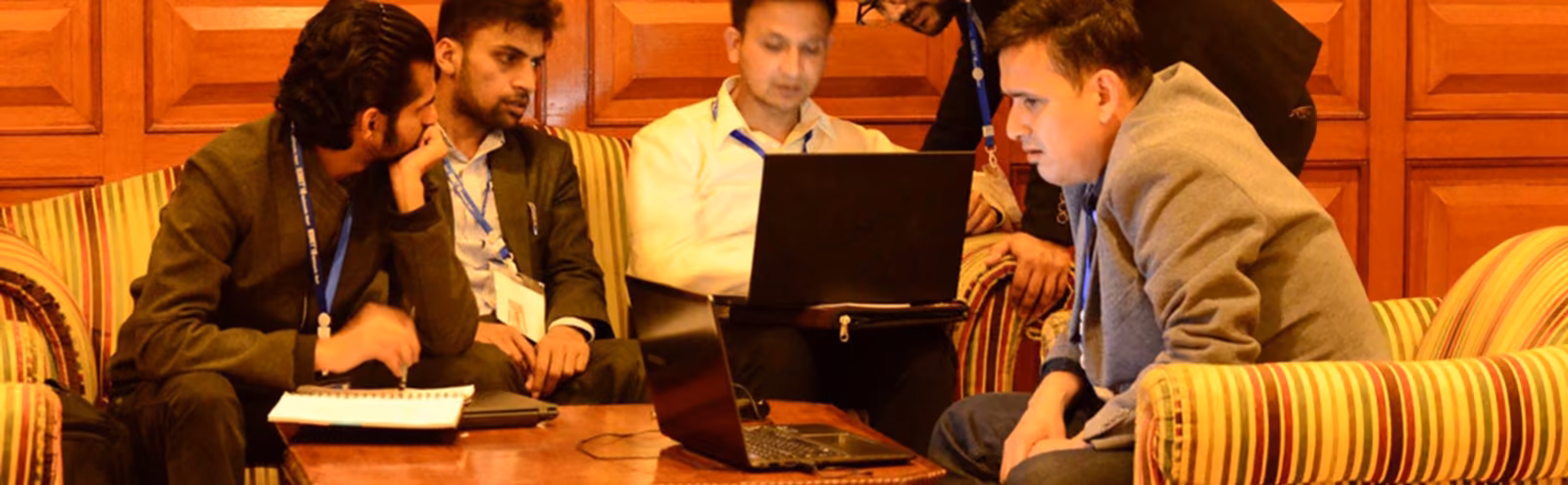 Students round a laptop in a wood-panelled room, papers spread across the table