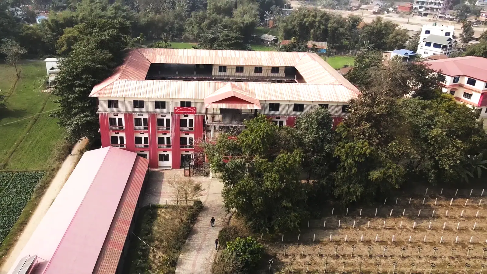 The college's red-roofed block from the air, fields and a river bank beyond it