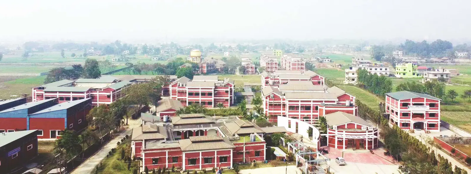 The university seen from the air: red-roofed blocks around a courtyard on flat open farmland