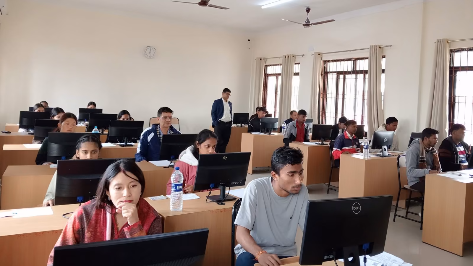Rows of students at desktop computers filling a long hall, sitting the computer-based entrance test