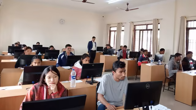 Rows of students at desktop computers filling a long hall, sitting the computer-based entrance test