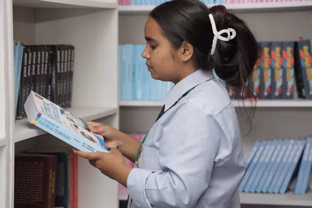 A student taking a book from the library shelves, more titles ranged behind her