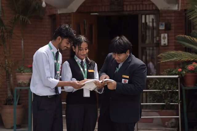 Three students reading a sheet of paper together in a doorway, plants along the step