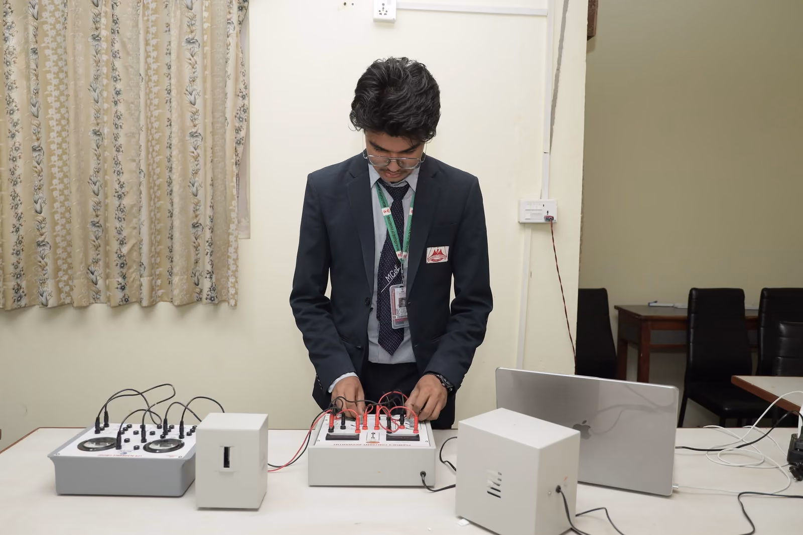A student wiring a trainer board on a laboratory bench, leads run across the top