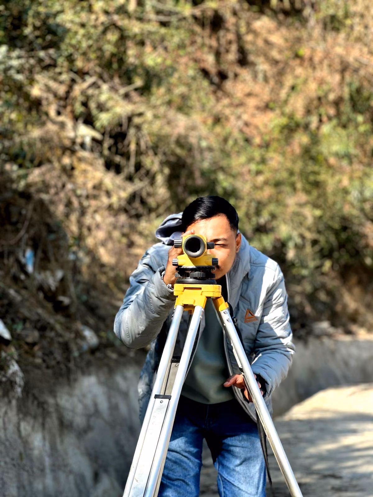 A student sighting through an automatic level on its tripod above a hill road