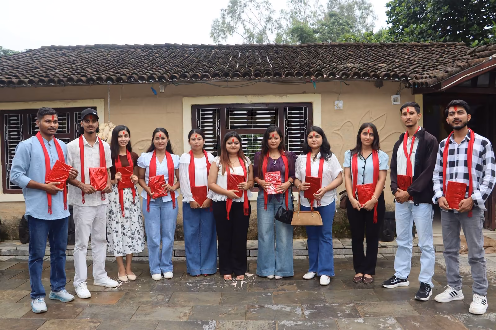 Students in red scarves lined up outside a low building with a tiled roof