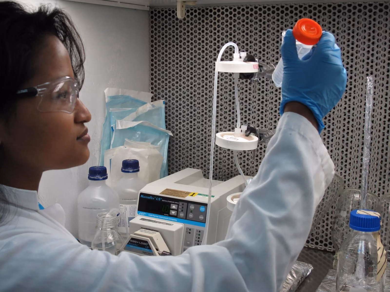 A student in goggles and gloves working at a lab bench of bottles and apparatus
