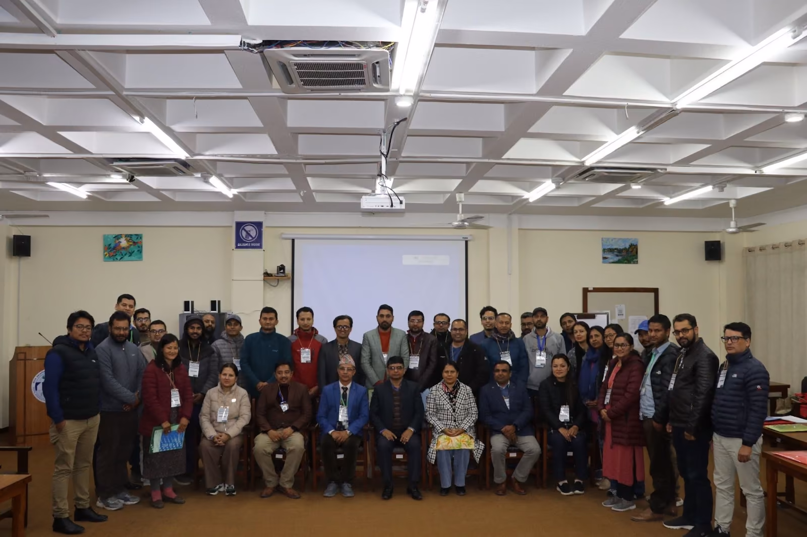 A large group photographed standing and seated in the college hall, conference lanyards on