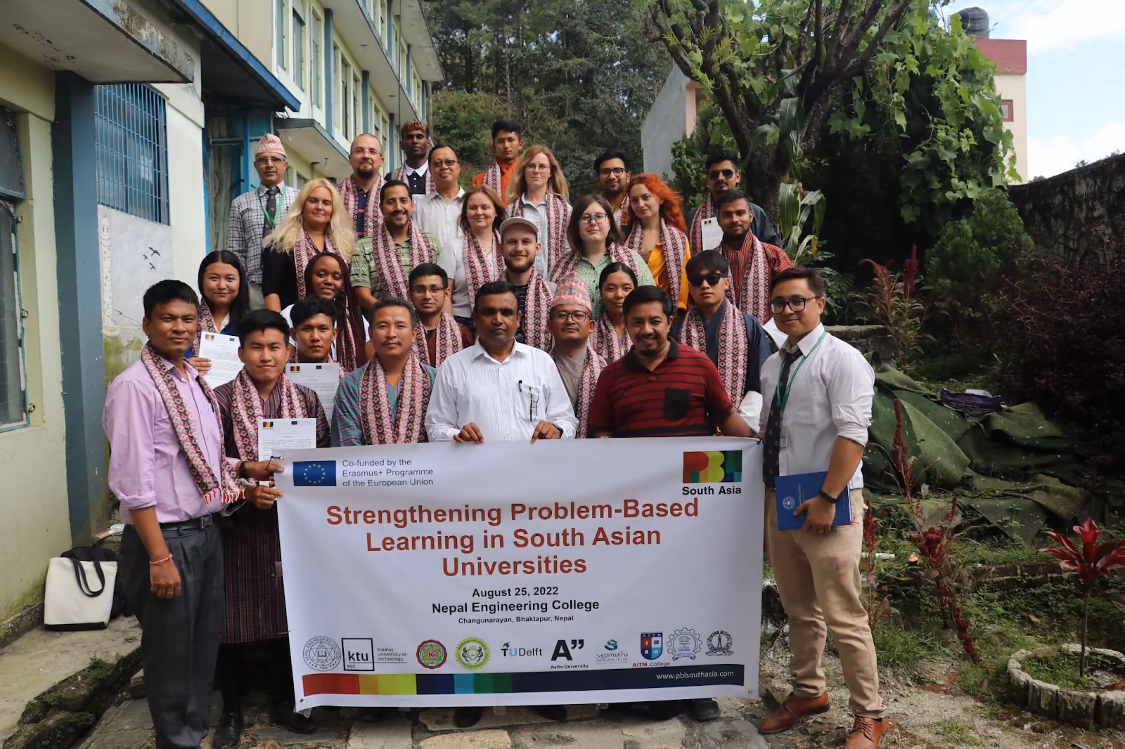 A workshop group holding its banner outdoors, a college block and trees behind them