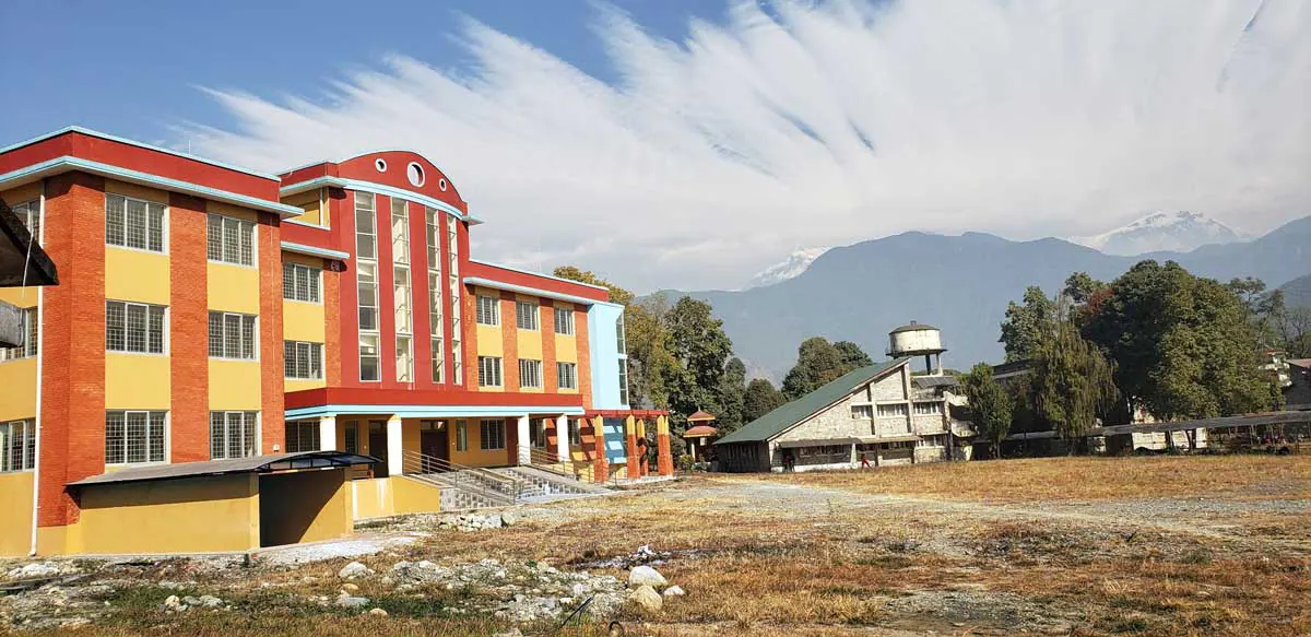 A campus block with a red roofline, snow mountains on the skyline behind the open field