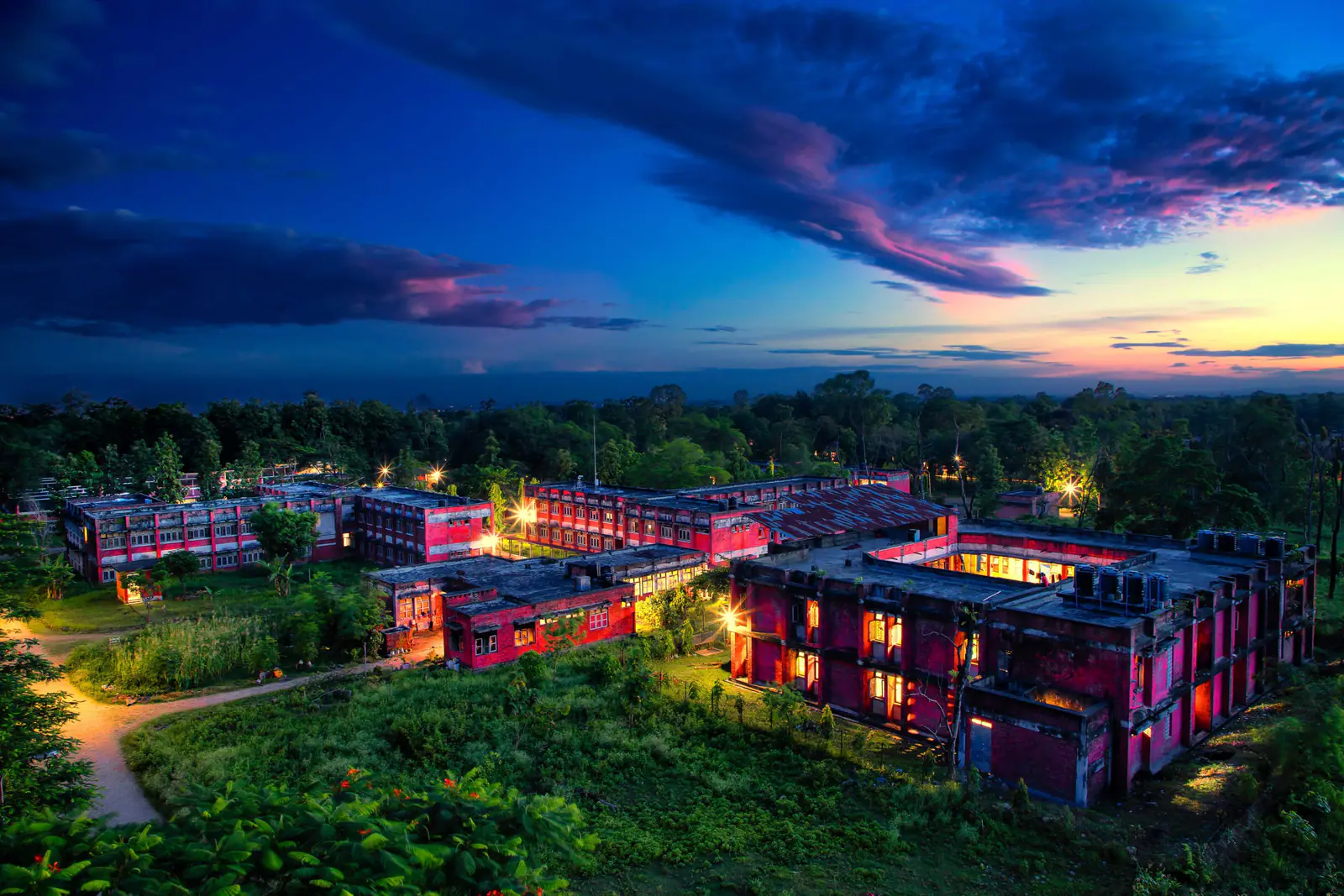 The campus from the air at dusk, its lit blocks laid out among trees under a red sky